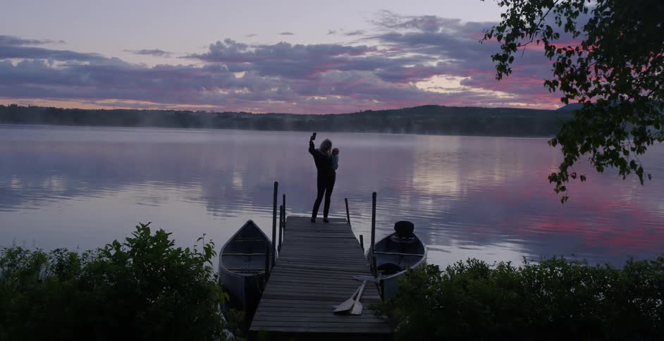 Person holds a baby standing on a dock by a lake