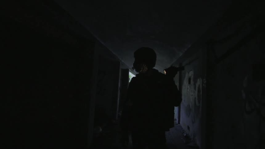 Silhouette of a person walking down a dark hallway with a flashlight in hand
