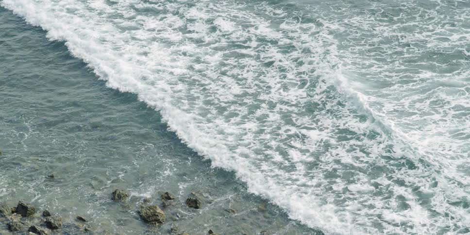 The waves slowly move towards the rocks on the shore