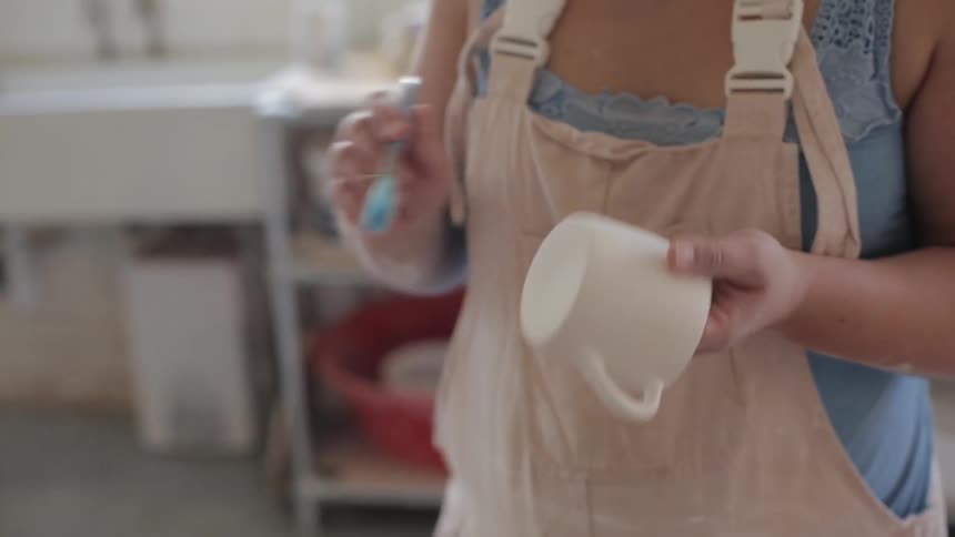 A woman brushing a clay mug with a brush