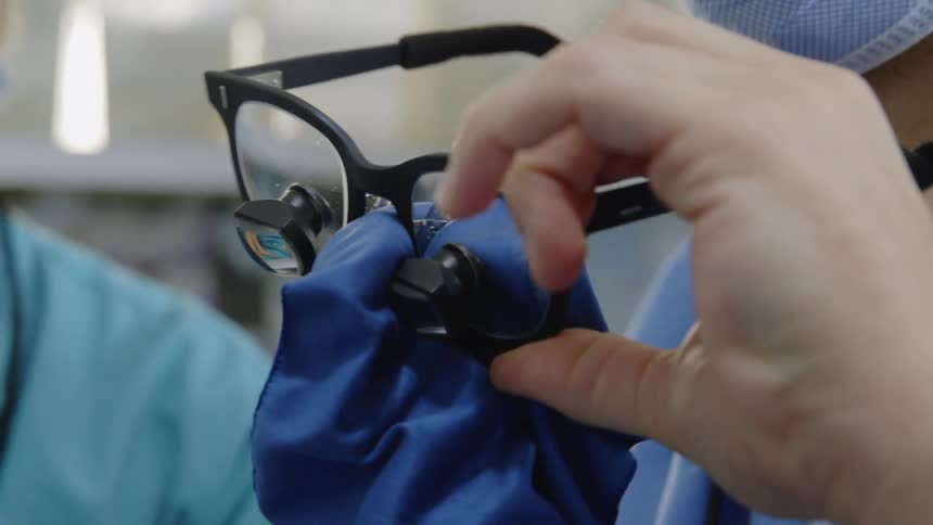 A surgeon cleans their glasses