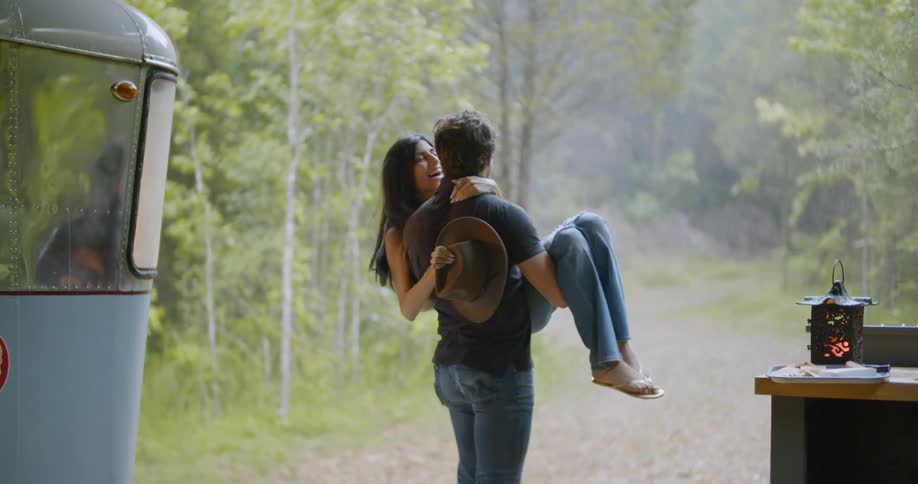Man lifts woman next to a camper