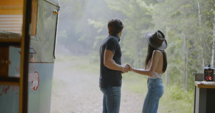 Man and woman hold hands outside while they watch the rain fall