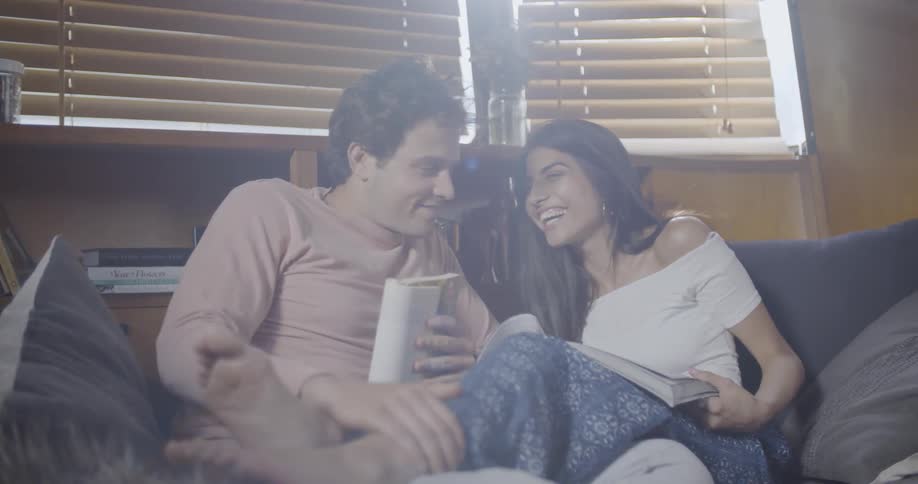 A man and woman are on the couch reading books and the man is rubbing the feet of the girl