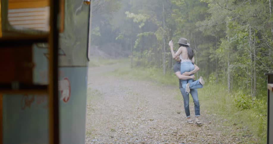 Man holding woman and walking outside as it rains
