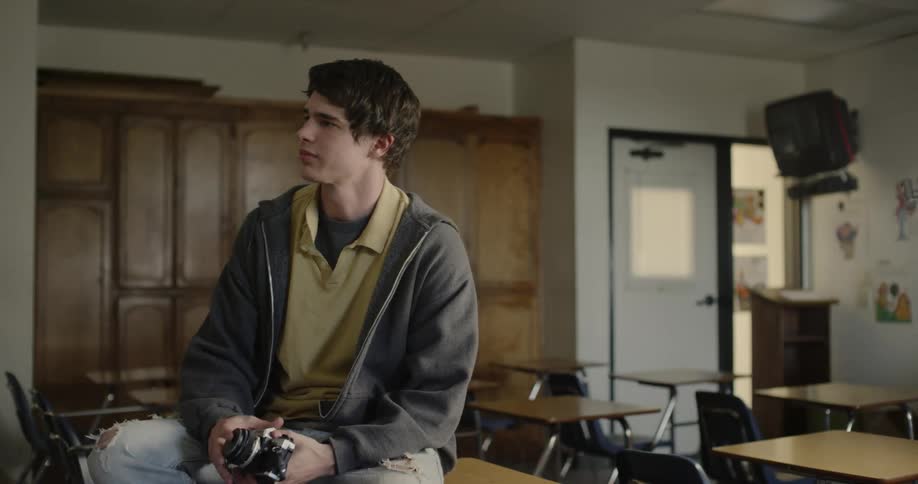A young man sits on a school desk