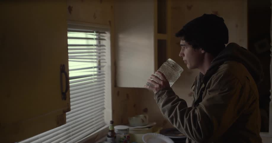 A man stands over a sink covered in dishes and gets water