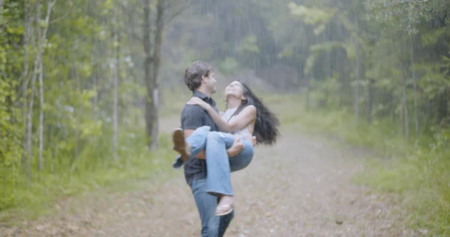 A man spins around with a woman in his arms in the rain