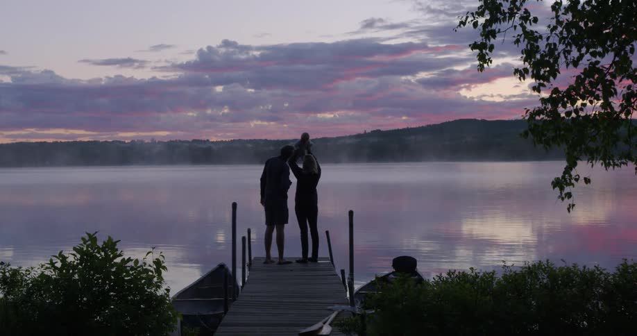 A family stands on a lake dock at sunset