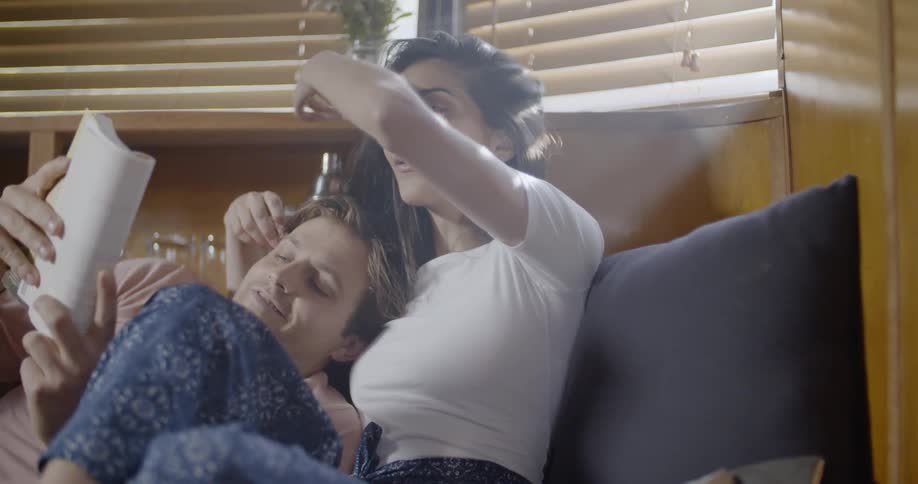 A couple read and cuddle on a bed during the day