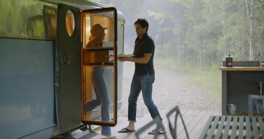 Woman exits camper and hands plate to man