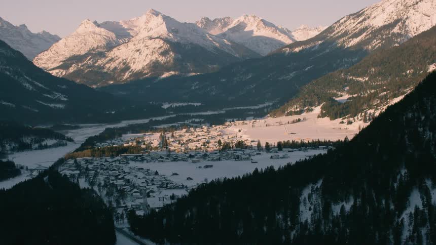Trees cover the snowy valley between mountains