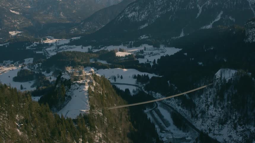A castle sits on top of a mountain that has a long rope bridge connecting it to other mountains