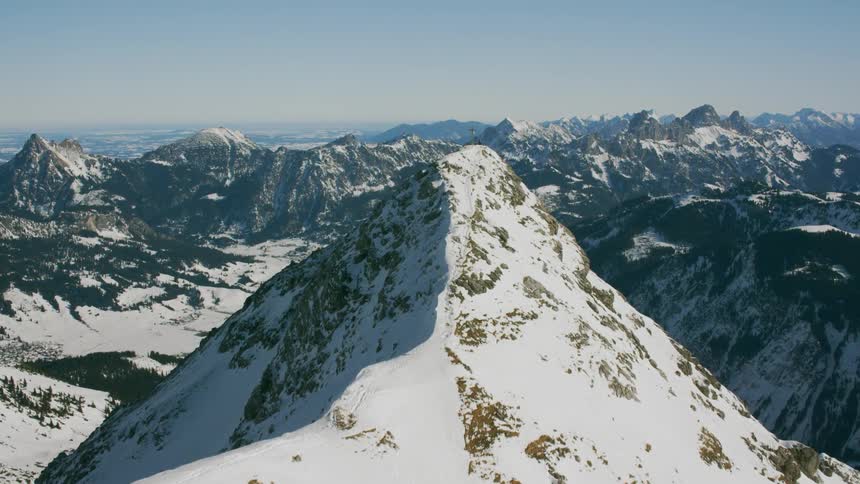 A cross sits perched on a snowy mountain peak