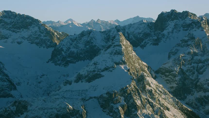 Snow blankets the slopes of a mountain range on a sunny day
