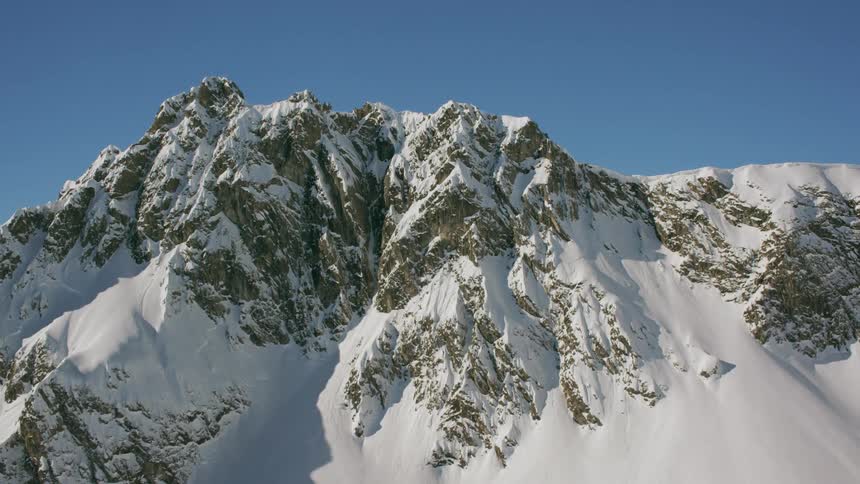Snow blankets the peaks and slopes of a mountain on a sunny day
