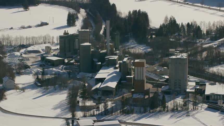 Smoke rises from a stack at a mill in a snow-covered village during the day