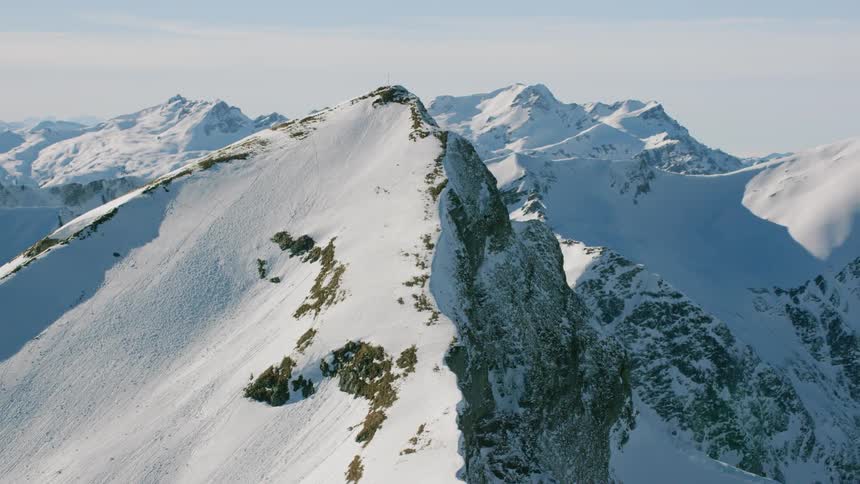Snow blankets the slopes of a mountain range on a sunny day