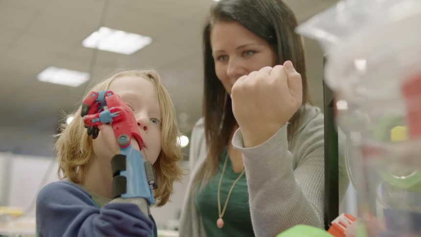 A small child and a mother are building a toy robot hand