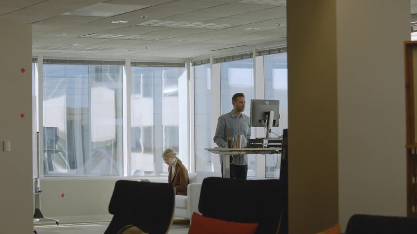 A man is standing and working at a computer in an office during the day