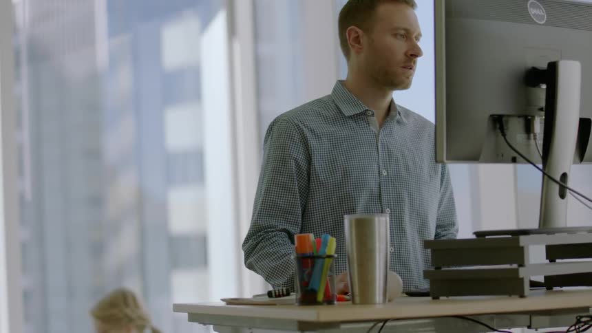 A man works in an office at a stand up desk