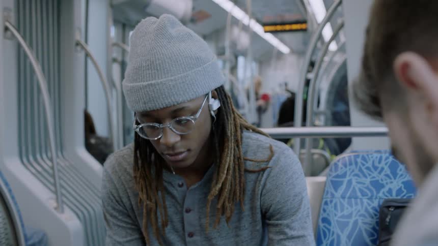 A man riding on a subway train leans back in his seat