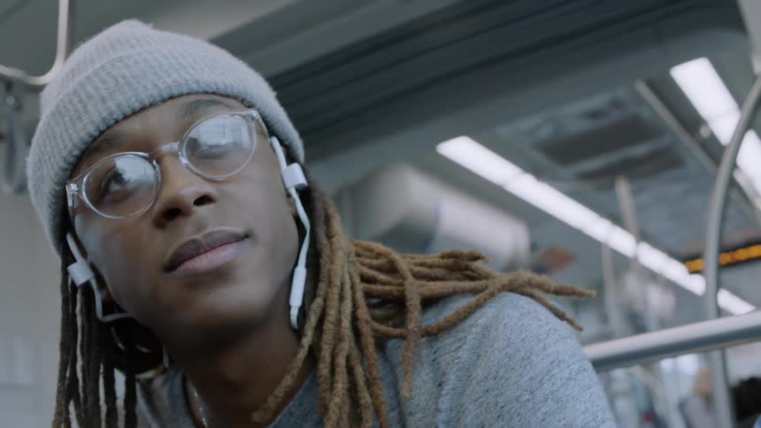 A mean with headphones on rides on a subway train