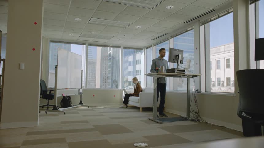 A man is standing working at a computer in an office during the day