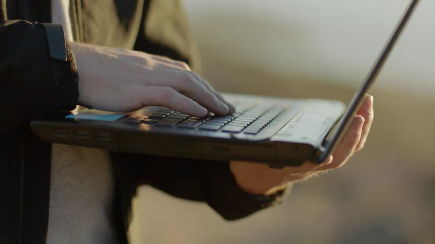 A man is standing outside using a laptop during the day