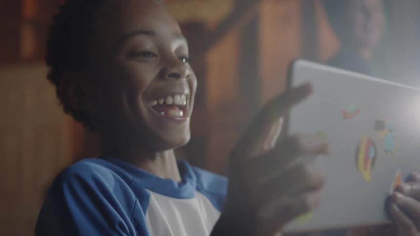 A young boy laughs at his tablet