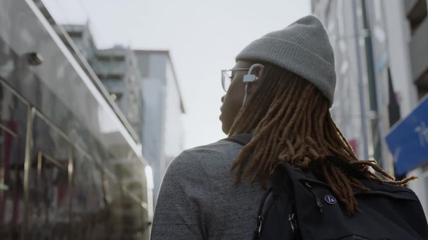 Man standing on a large city street wearing headphones and looking around