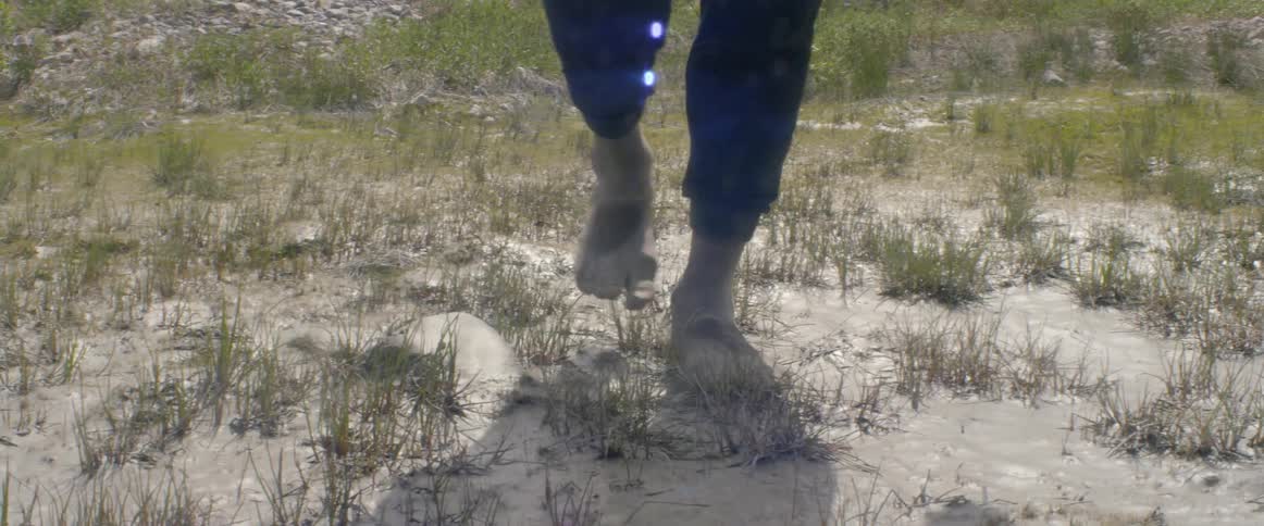 Barefoot person walks on a weedy patch of land