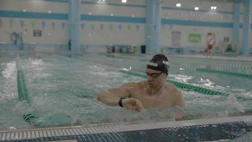 Man swimming in lap pool and looking at his time on watch