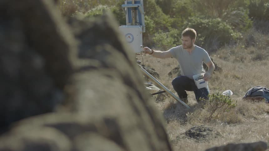 A man is taking samples from a device out in the desert