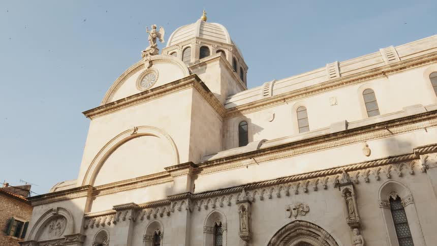 A flock of birds is fluttering in the sky above a domed old building during the day