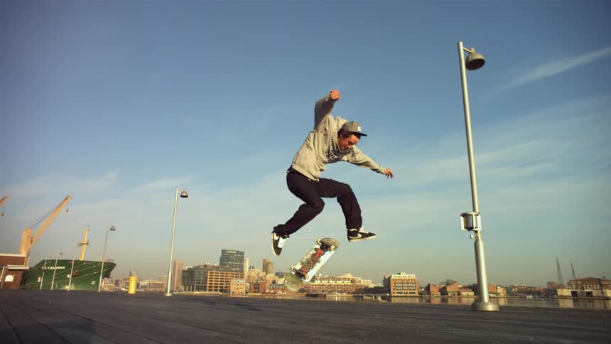 A man rides backwards on a skateboard and jumps into the air