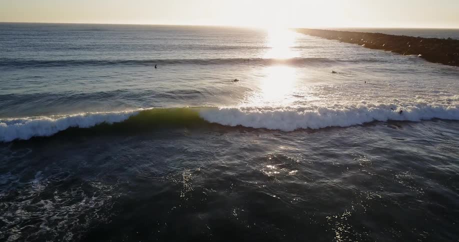 People are surfing around in the water at sunset