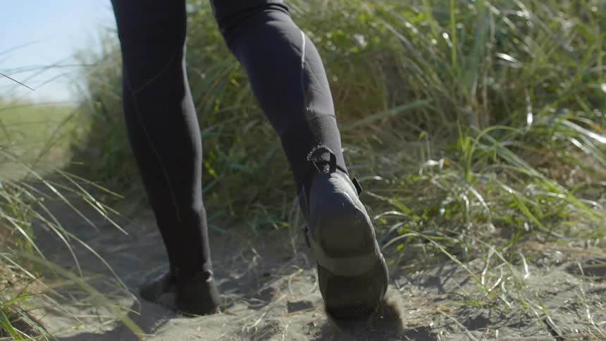 A person wearing a wet suit walks towards the shore