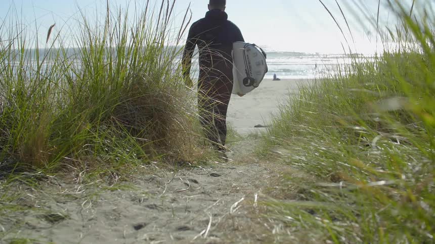 Surfer walks on beach with surfboard