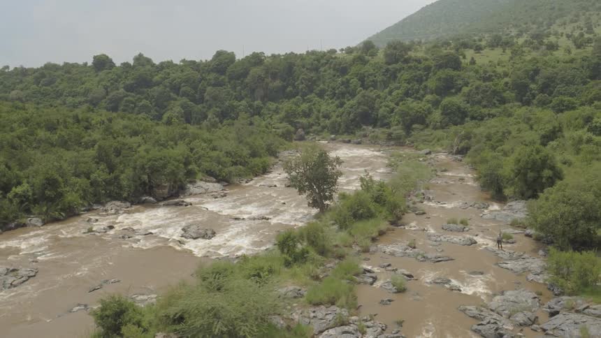 A man is climbing over the rapids in the wilderness below
