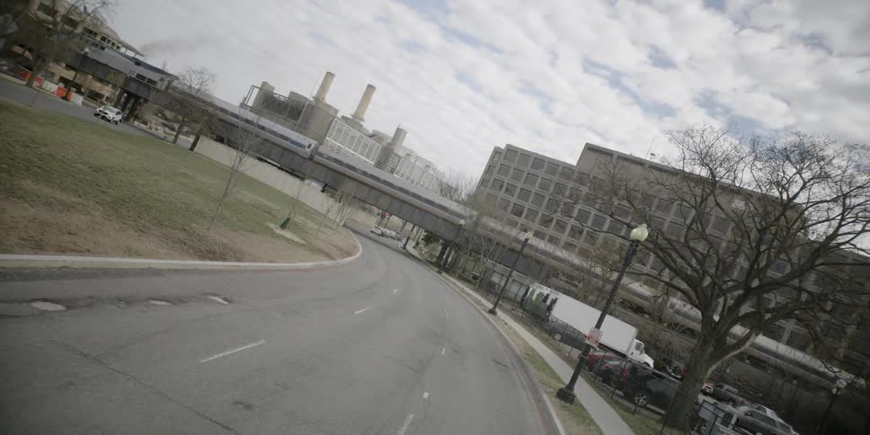 A train is running above a street with some industrial buildings in the background