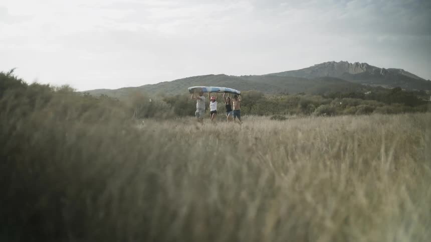 People carry a kayak across a grassy field
