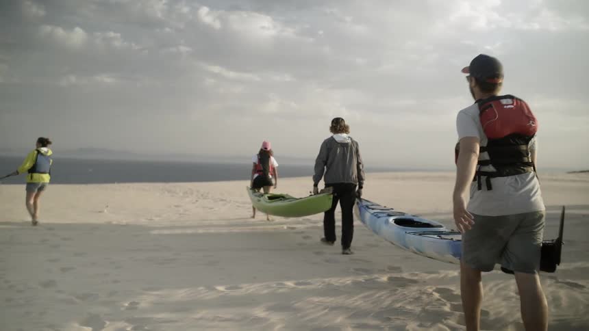 People carry canoes on the beach towards the water