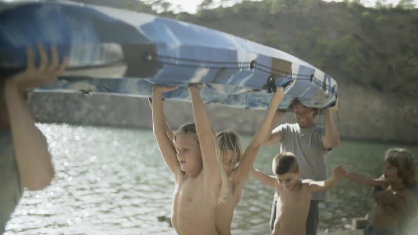 A family carries a kayak next to a lake