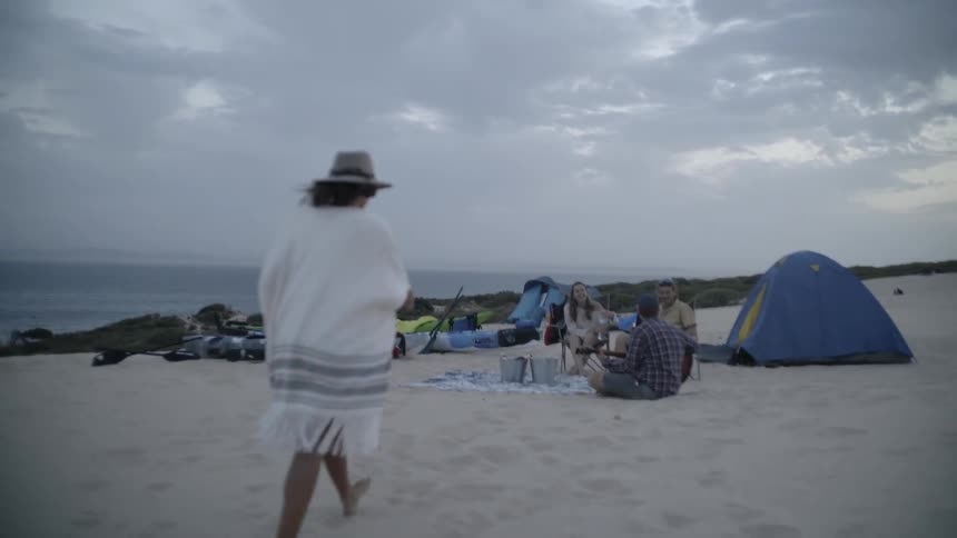 A woman is walking over the beach sand to a group of friends at a campsite