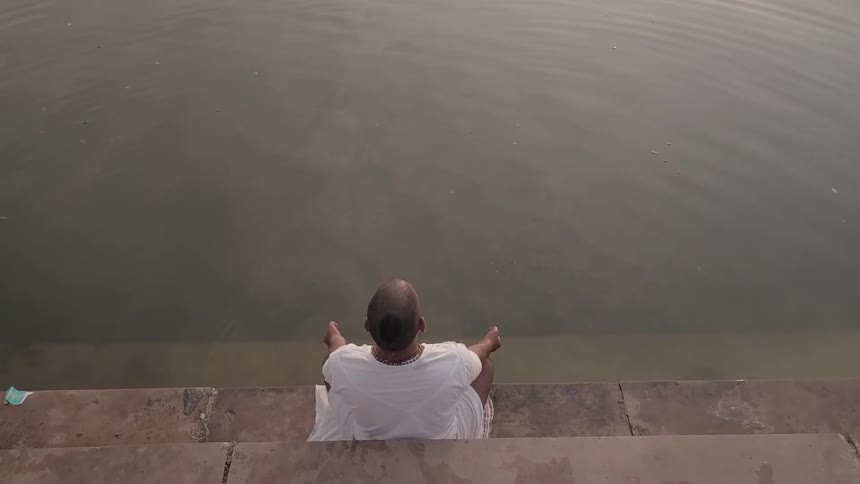A man is sitting on the edge of a river with his feet in the water