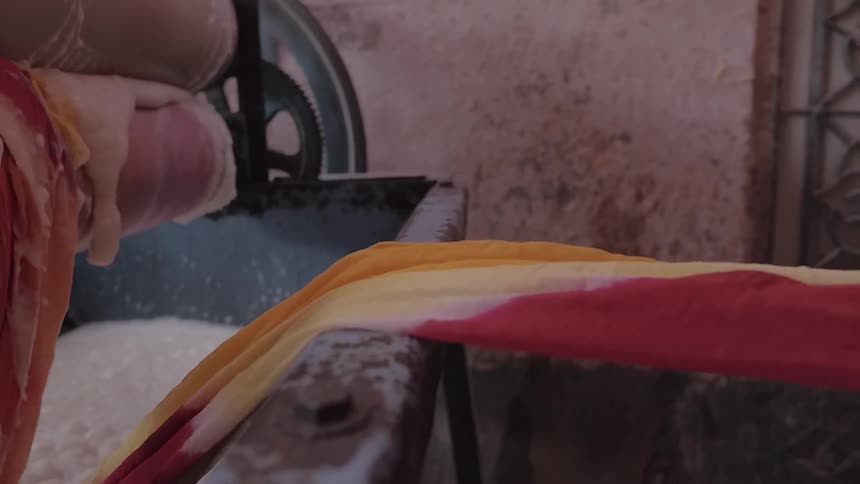 Fabric is being fed into a wash basin with a roller inside a building during the day