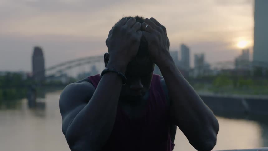 A black man holds his head in his hands outside in the city