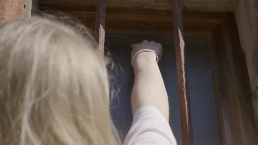 Woman reaches through window bars and writes on the window