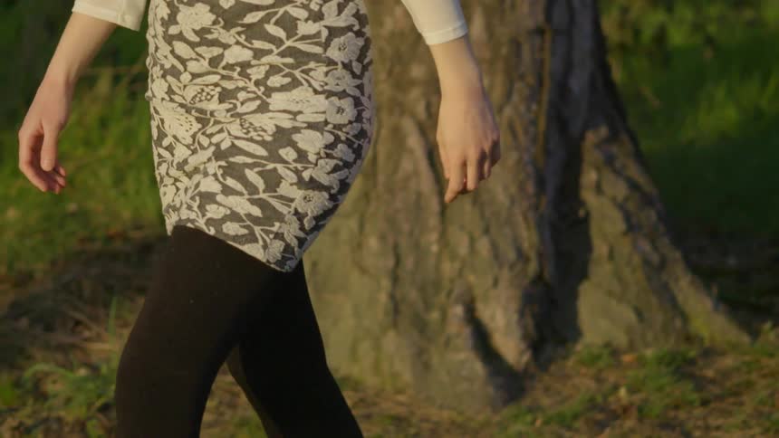 A woman is walking past a large tree on a sunny day